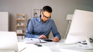 Male accountant in grey shirt calculating income and expenses to keep clean bookkeeping records for a WItney business.